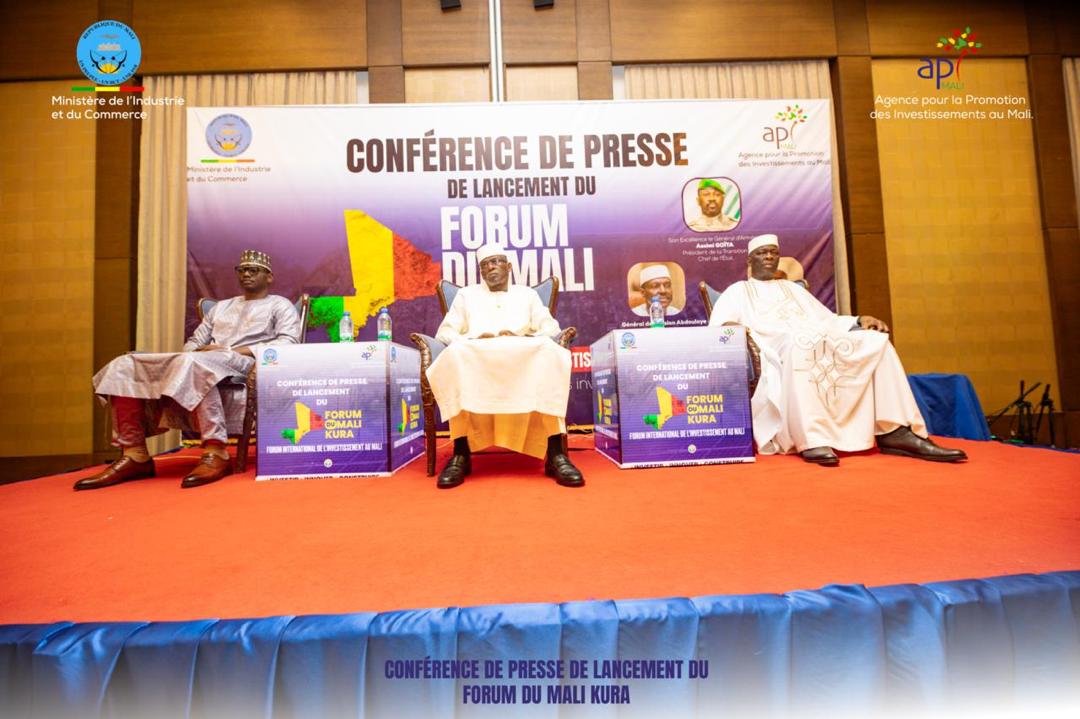 Stage of the Mali Kura Forum launch press conference: three officials in grand boubous seated on a red-carpeted platform between two lecterns in the forum’s colours, in front of the “Launch press conference of the Mali Forum” banner.
